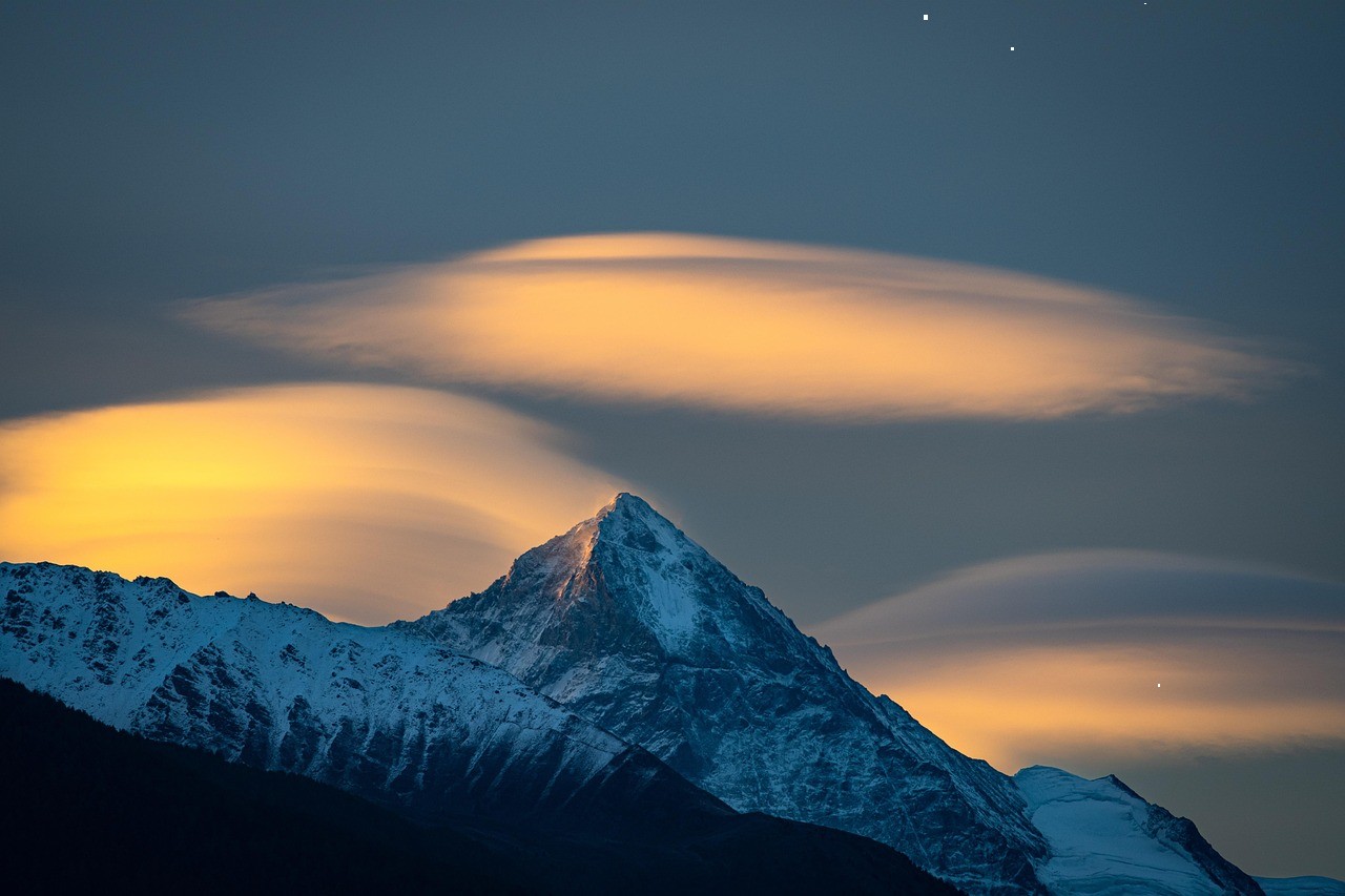 Snowy mountain peak with glowing lenticular clouds at dusk.